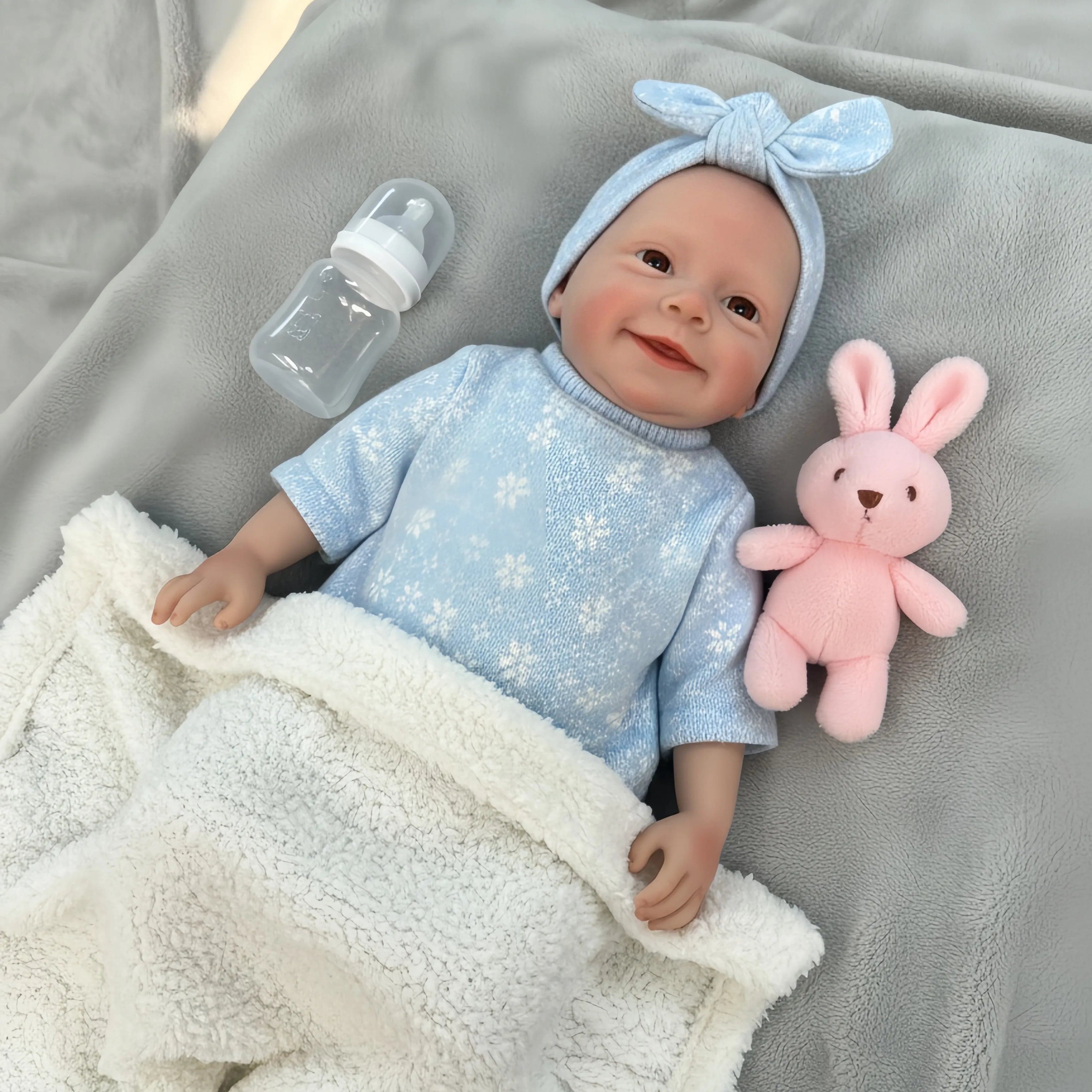Finished reborn doll in a powder-blue knit sweater and matching bow headband, resting on a cream fleece blanket beside a plush bunny.